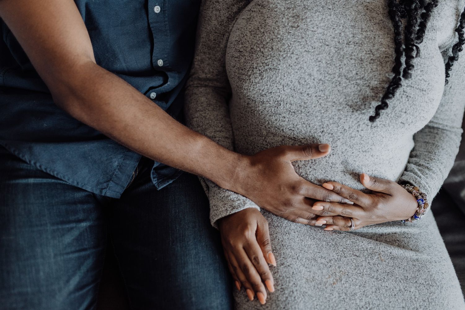 Couple tenderly holding hands on pregnant belly, wearing casual clothes, maternity photo session.