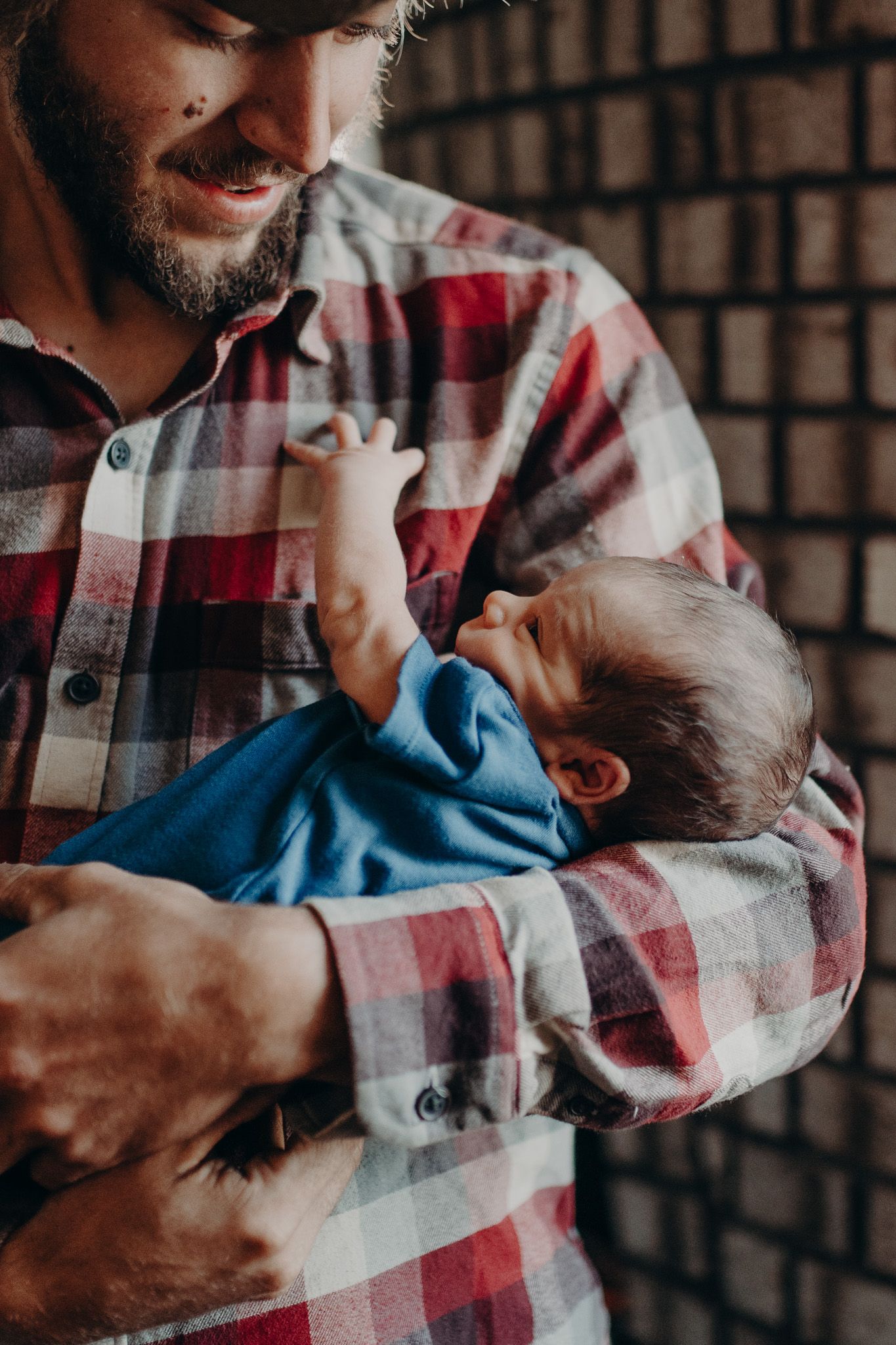 Smiling bearded man in plaid shirt tenderly cradling a newborn baby dressed in blue.