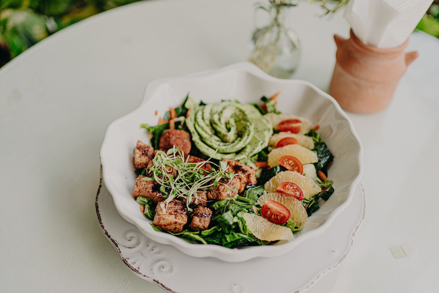 A vibrant salad bowl with grilled chicken, cherry tomatoes, greens, and sliced avocado served in a white scalloped dish.