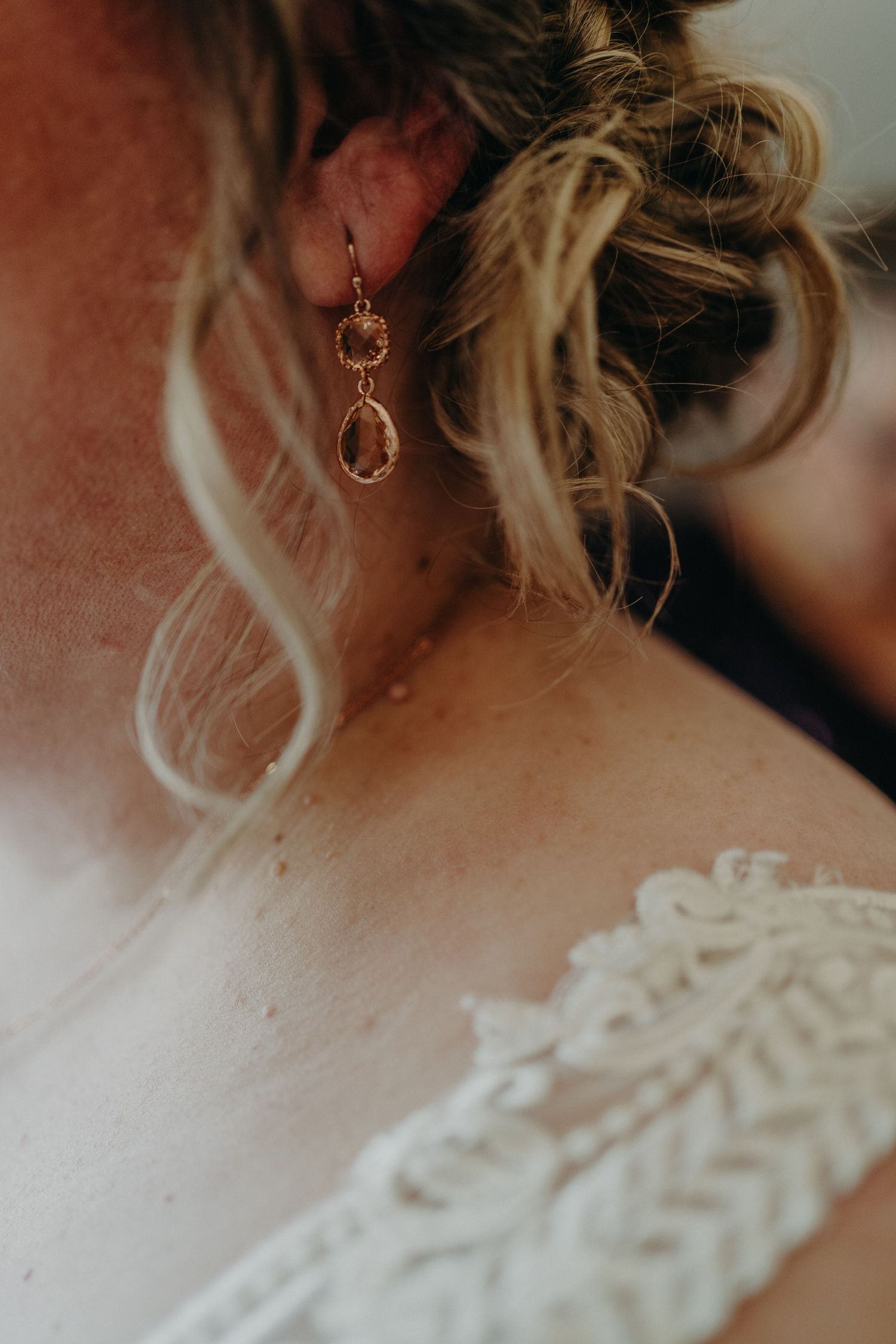 Close-up of bride's elegant rose gold drop earring with updo hairstyle and lace dress detail.