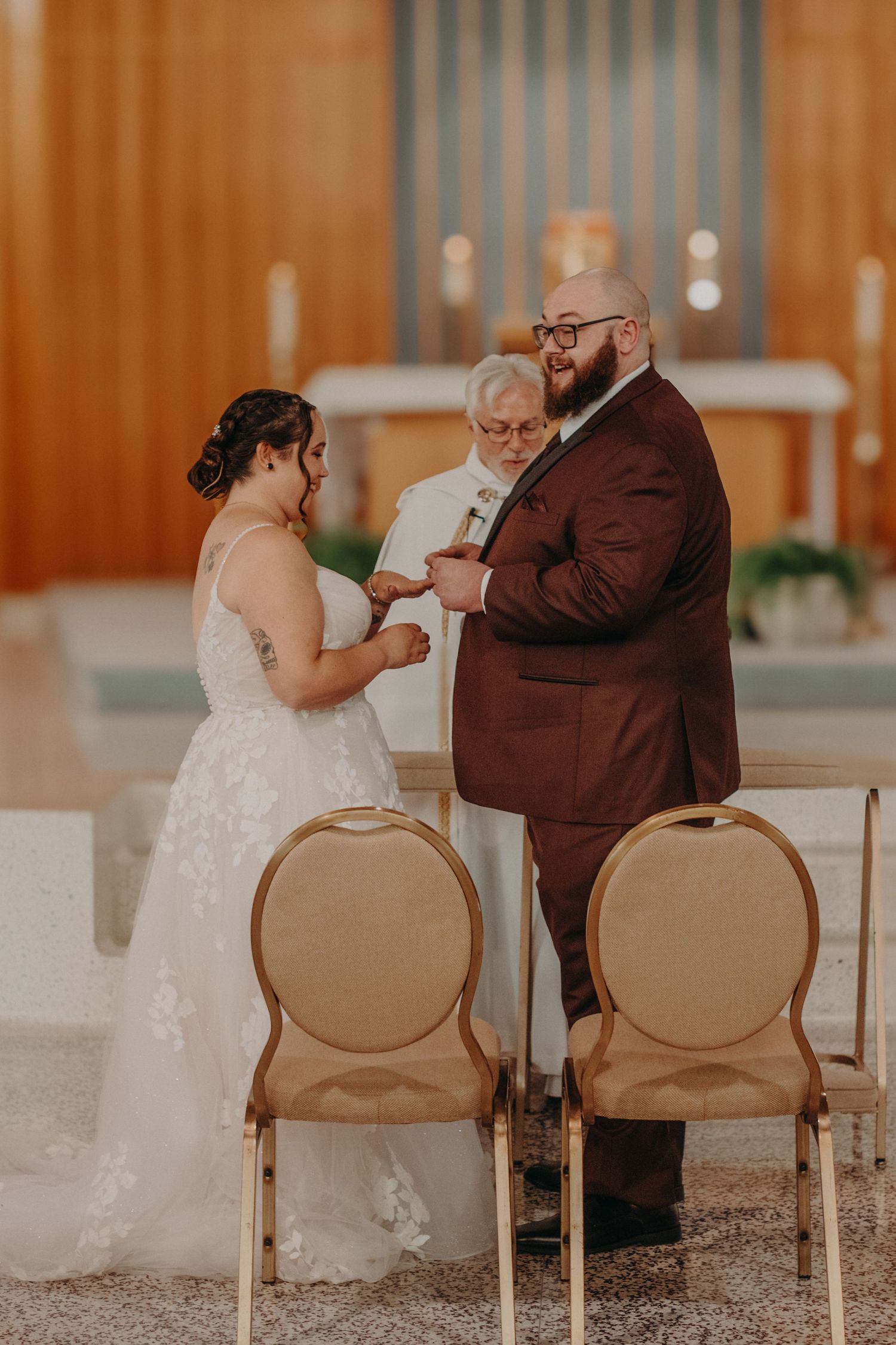 Bride and groom exchange rings at church altar with officiant during indoor wedding ceremony.