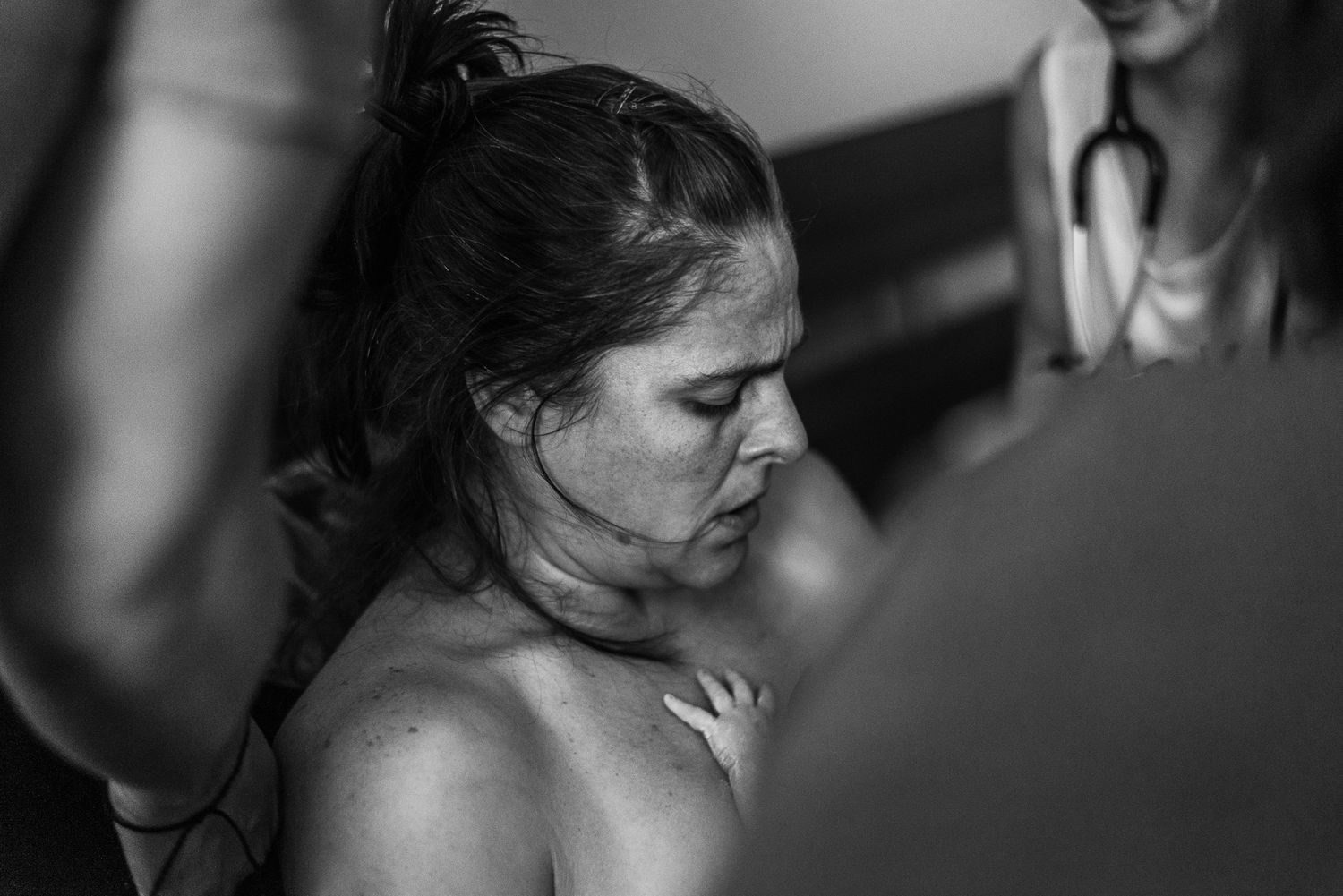 Black and white photo of a woman in labor, sweating and focused, supported by medical staff during childbirth.