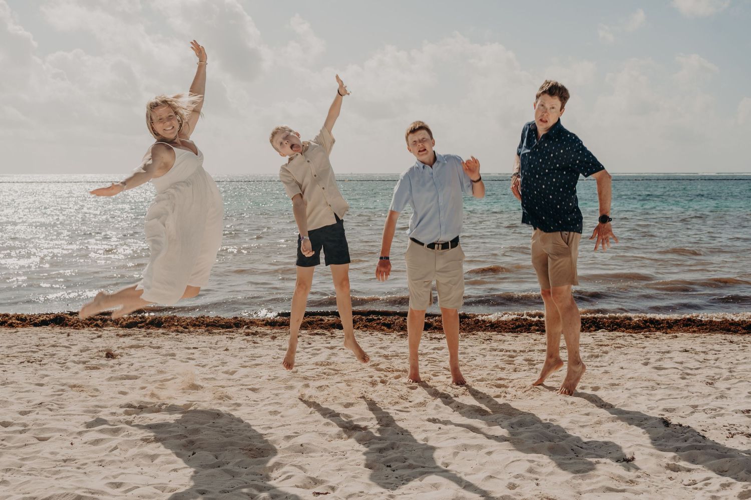 Four people jumping joyfully on a sunny beach with ocean waves in the background.