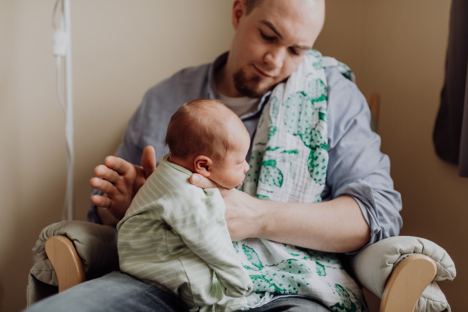 A father gently holds his newborn baby while seated in a chair, sharing a tender bonding moment.