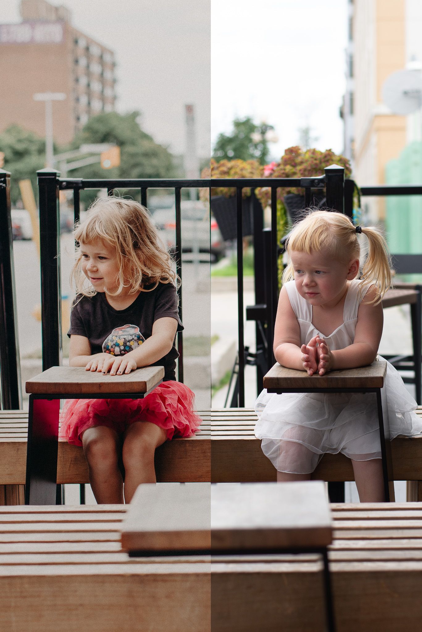 Two young blonde girls in colorful skirts sit on a wooden bench at an outdoor cafe terrace.