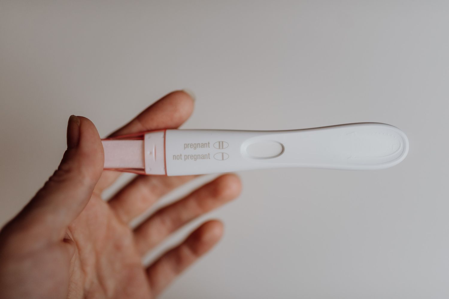Hand holding a white pregnancy test showing a single line, indicating a not pregnant result, on a gray background.