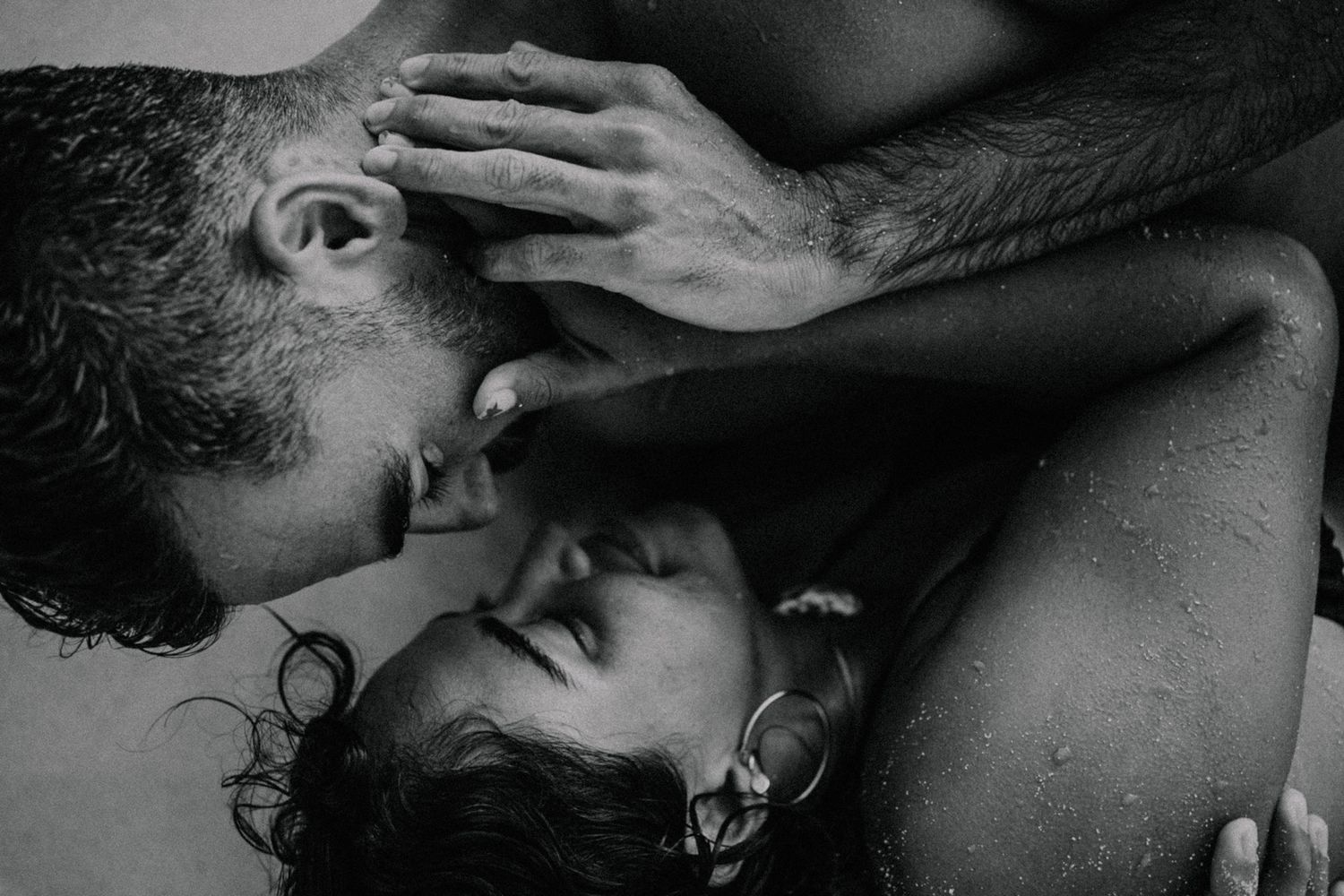 Black and white intimate couple portrait with man kissing woman in passionate romantic embrace.