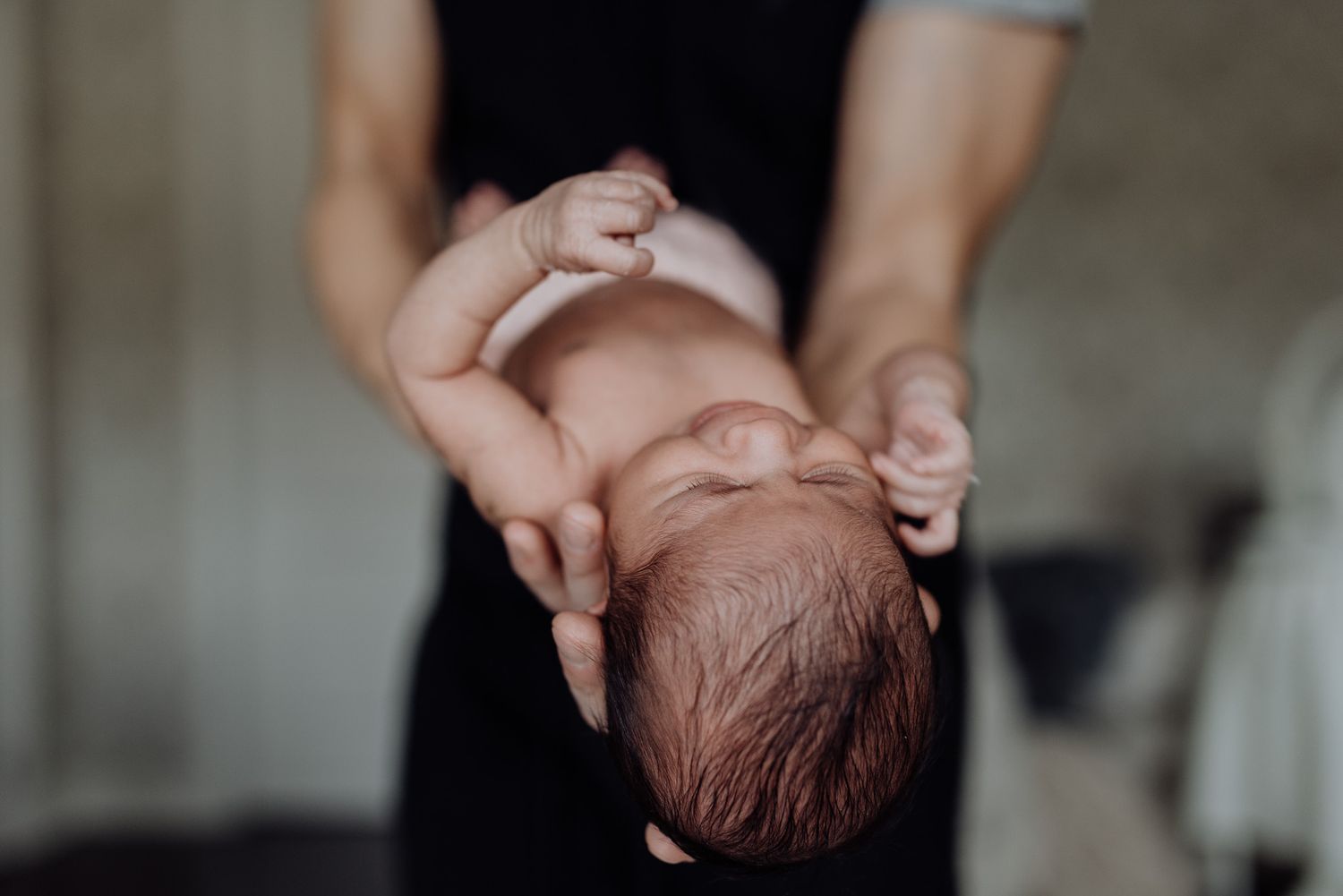 Adult hands cradling a newborn baby lying on its back, captured in soft natural light.