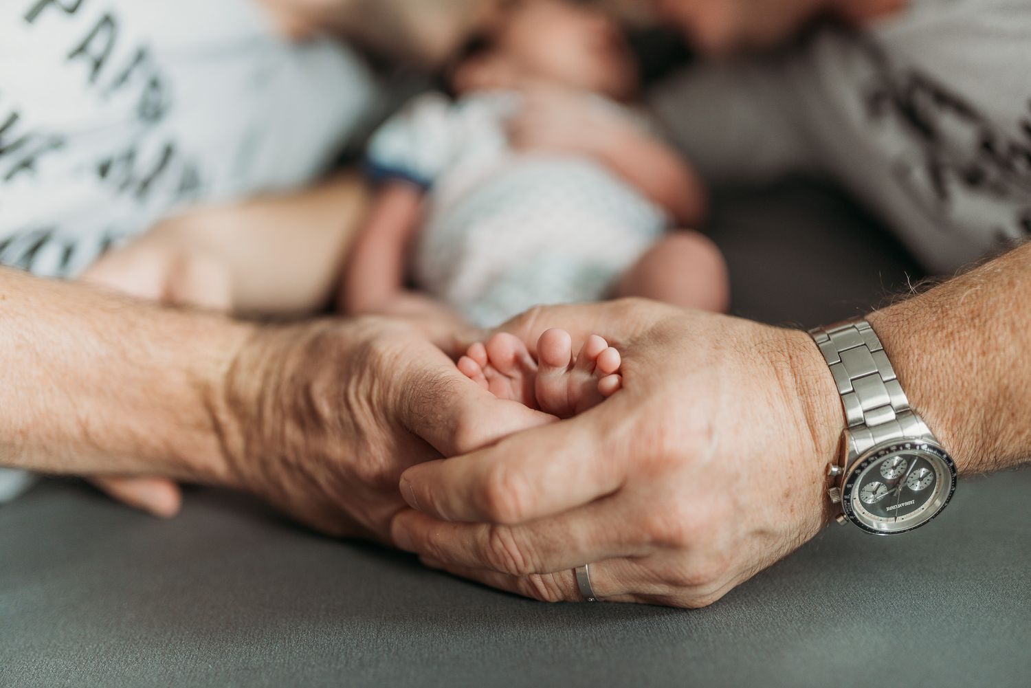 An adult tenderly holding a newborn baby's tiny feet, with a silver watch visible on their wrist.
