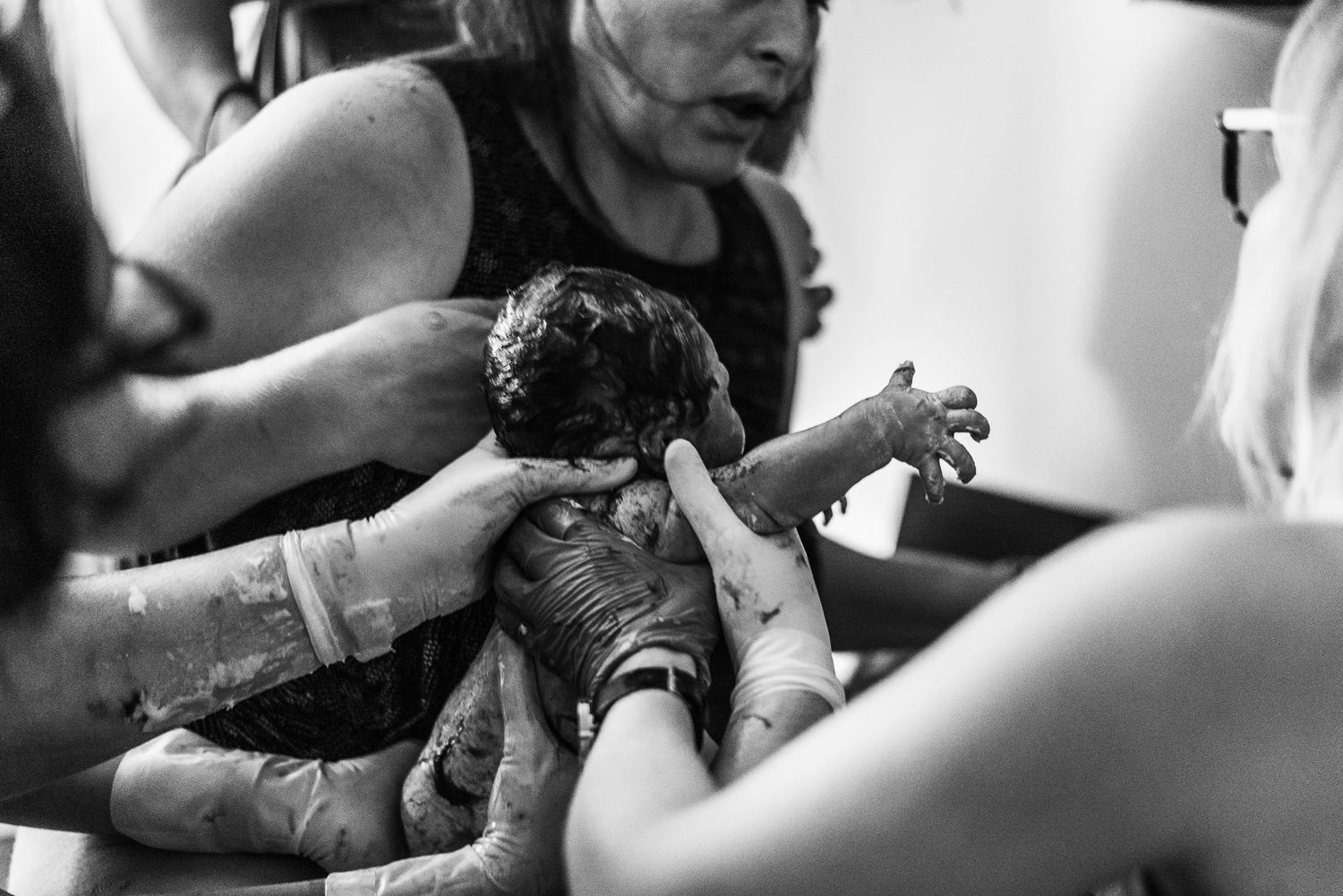 Black and white photo of a newborn baby being delivered, held by medical professionals during childbirth.