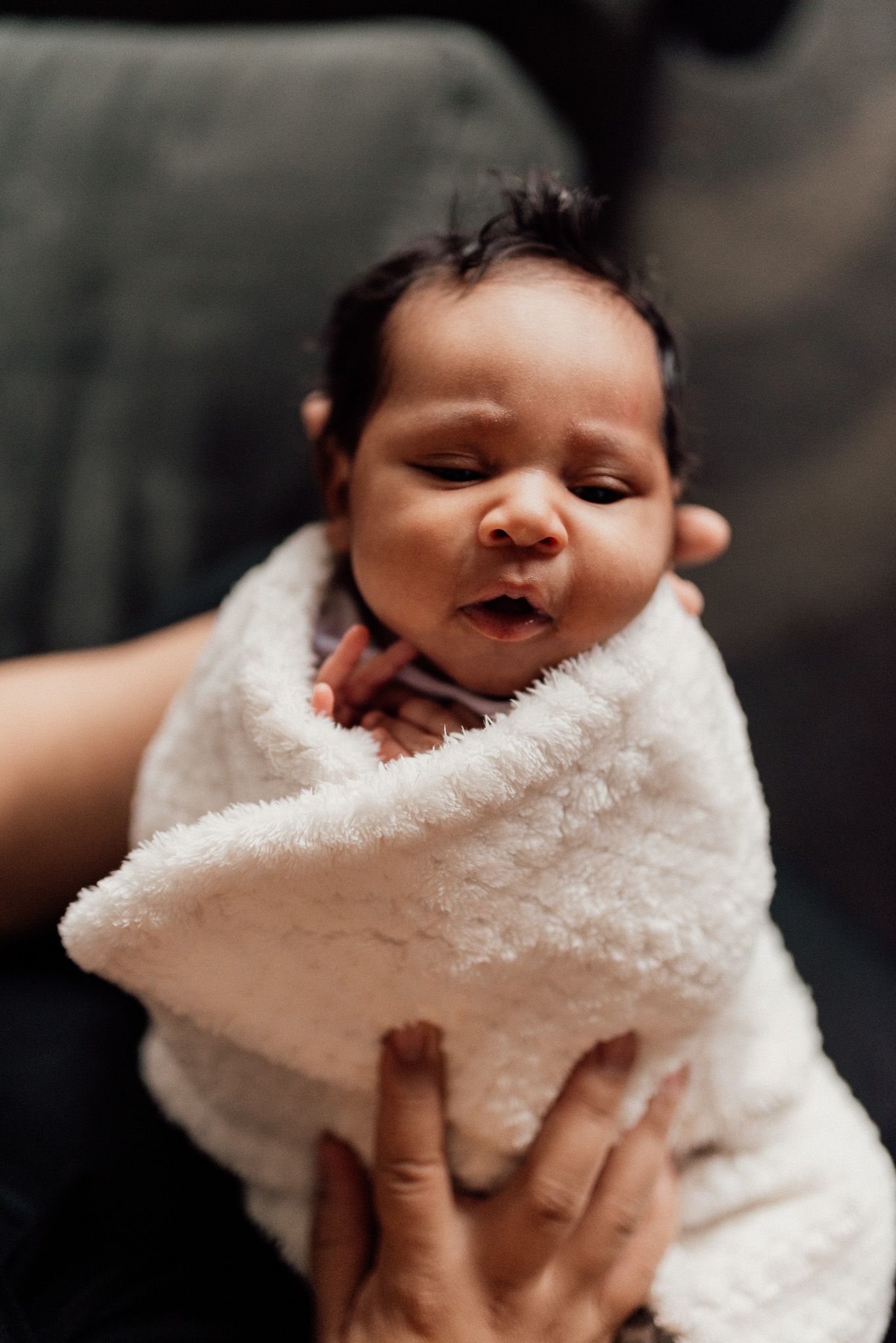A newborn baby swaddled in a soft white blanket being gently held by caring hands.