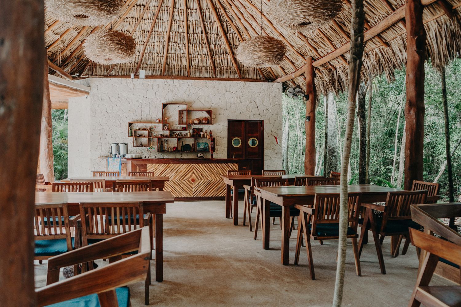 Rustic open-air restaurant with thatched roof, wooden tables, and lush jungle views in a tropical setting.