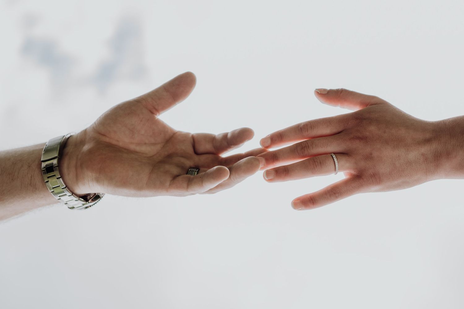 Close-up of bride and groom reaching hands toward each other showing wedding rings on white background.