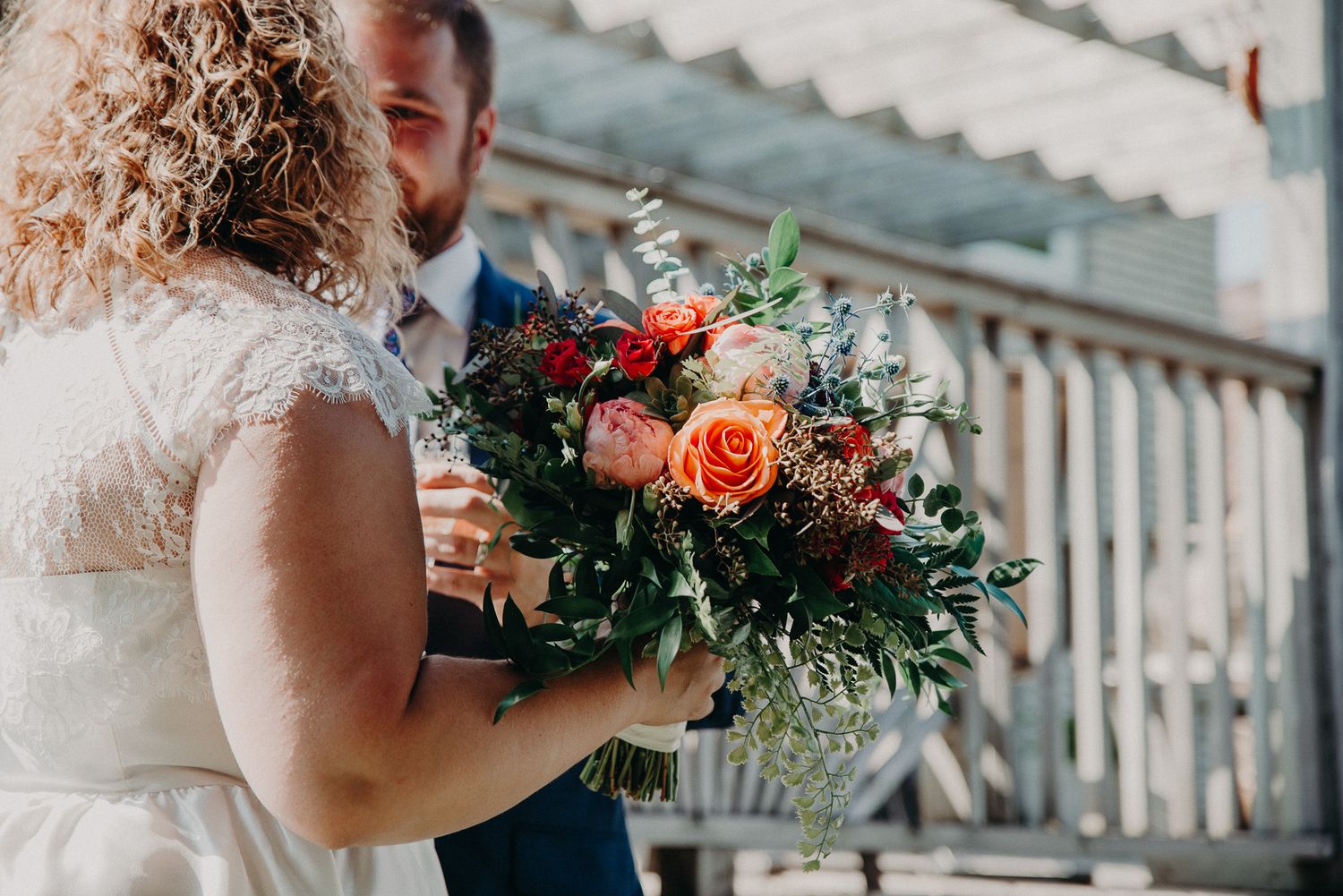 Bride and groom share a close moment with a vibrant orange and red bridal bouquet.