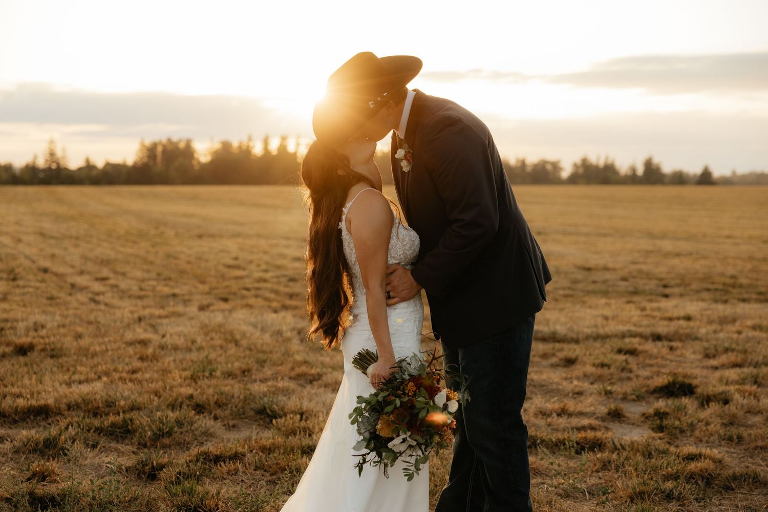 Bride and groom kissing at sunset in Oregon field, rustic wedding photography