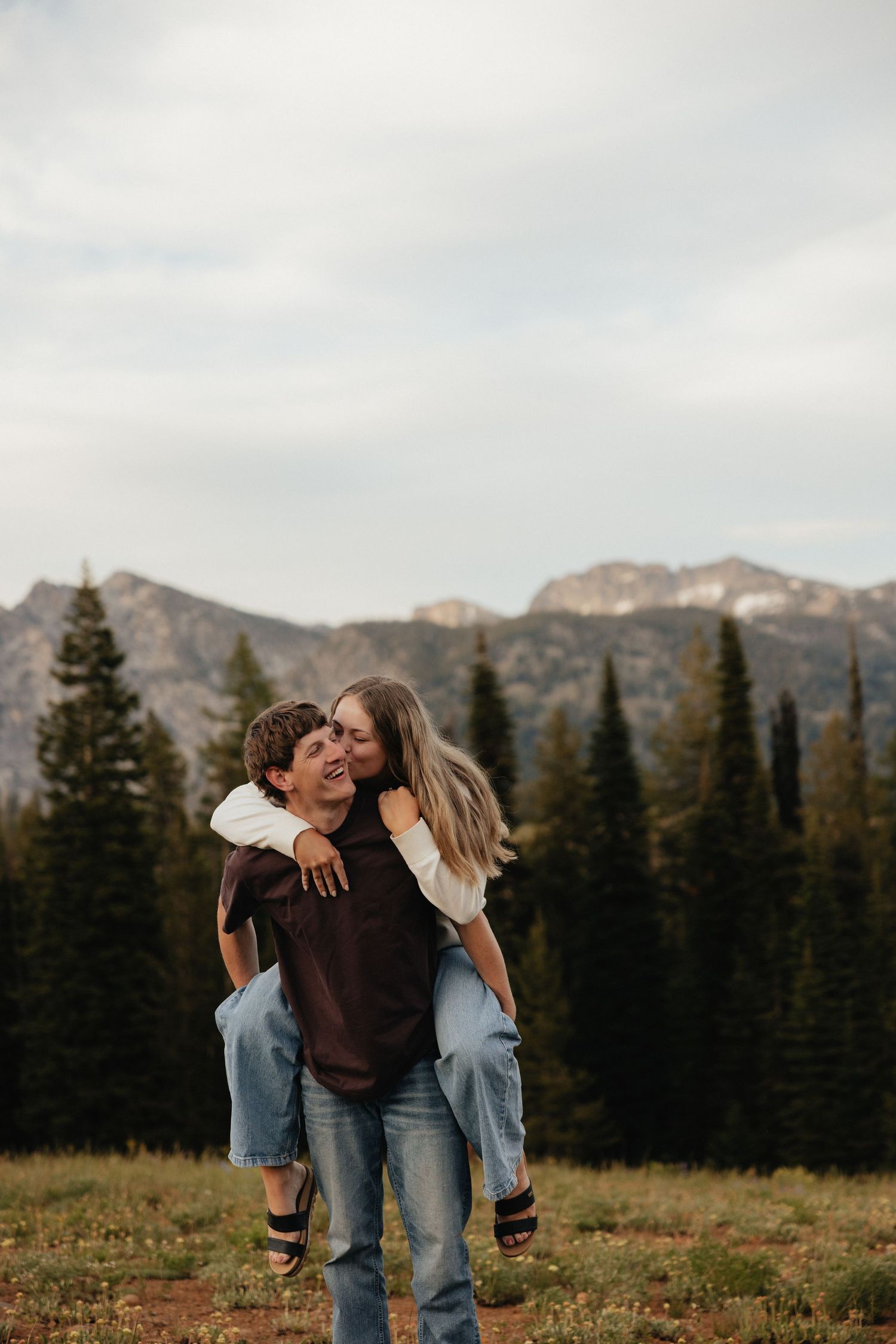 Joyful couple piggyback ride in Eastern Oregon mountains, lifestyle engagement photography