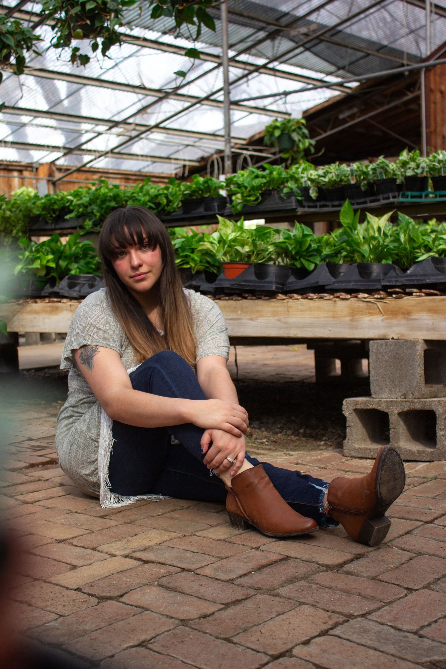 A girl sitting on the brick floor surrounded by plants in a greenhouse.