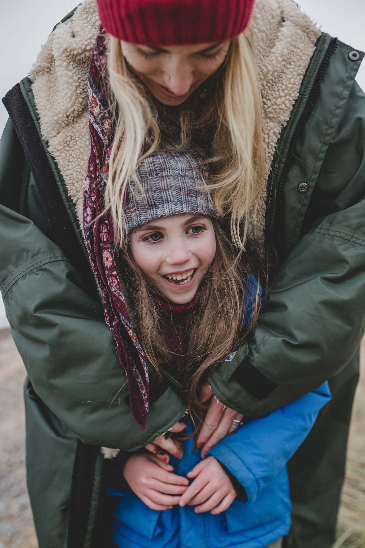 Two people in winter coats and knit hats sharing a warm embrace outdoors.