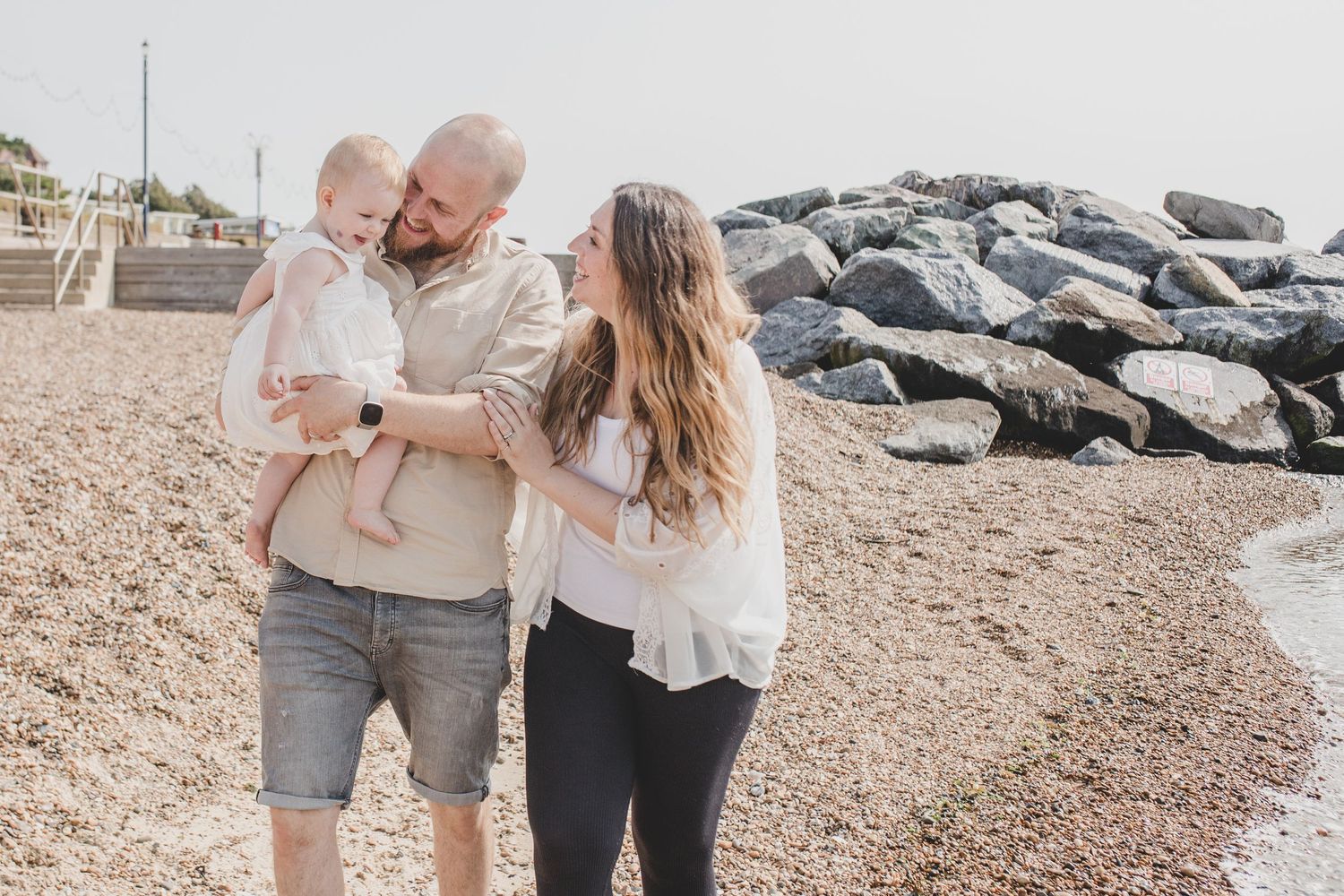 A couple shares a tender moment on a rocky beach shoreline on an overcast day.