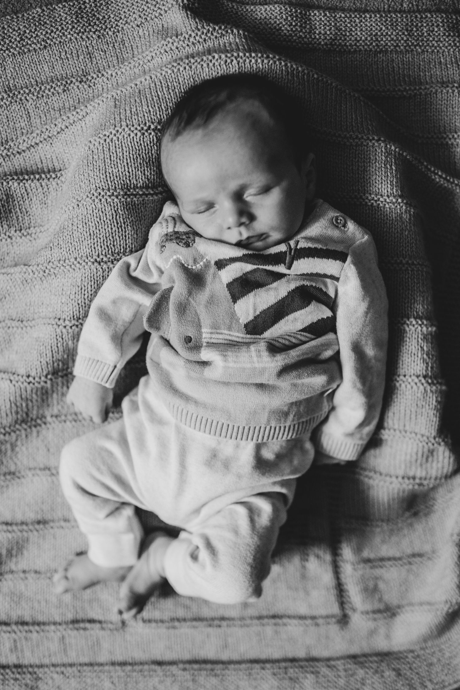 Sleeping newborn wearing striped sweater rests peacefully on textured blanket in black and white.