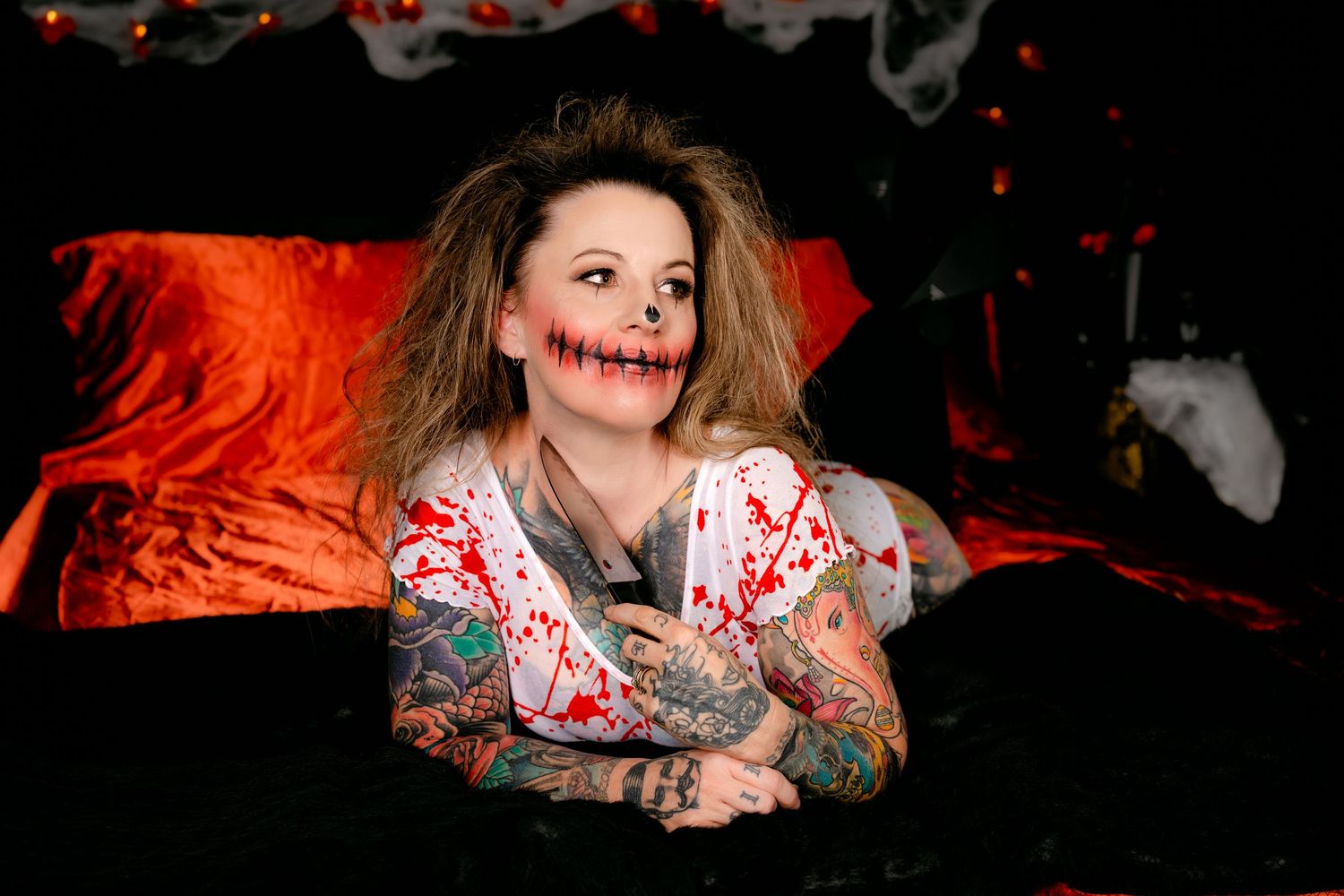 Person wearing white and red patterned clothing poses on dark background with dramatic lighting.
