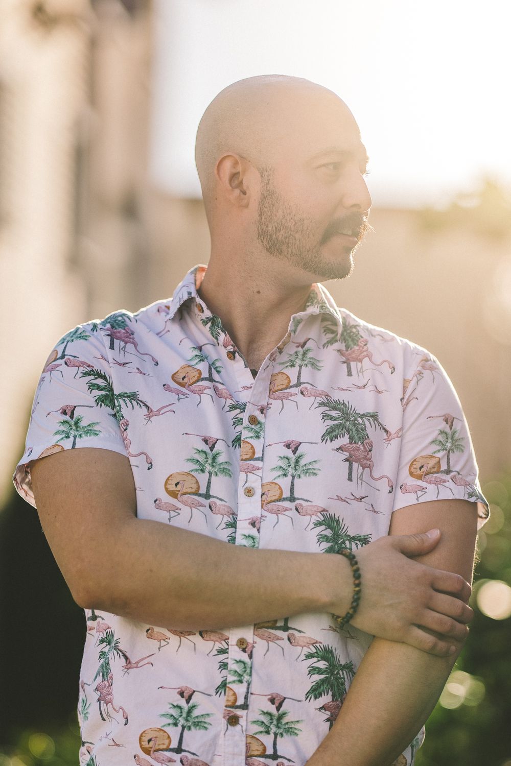 Person wearing a tropical print shirt with palm trees and flamingos in warm sunset light.