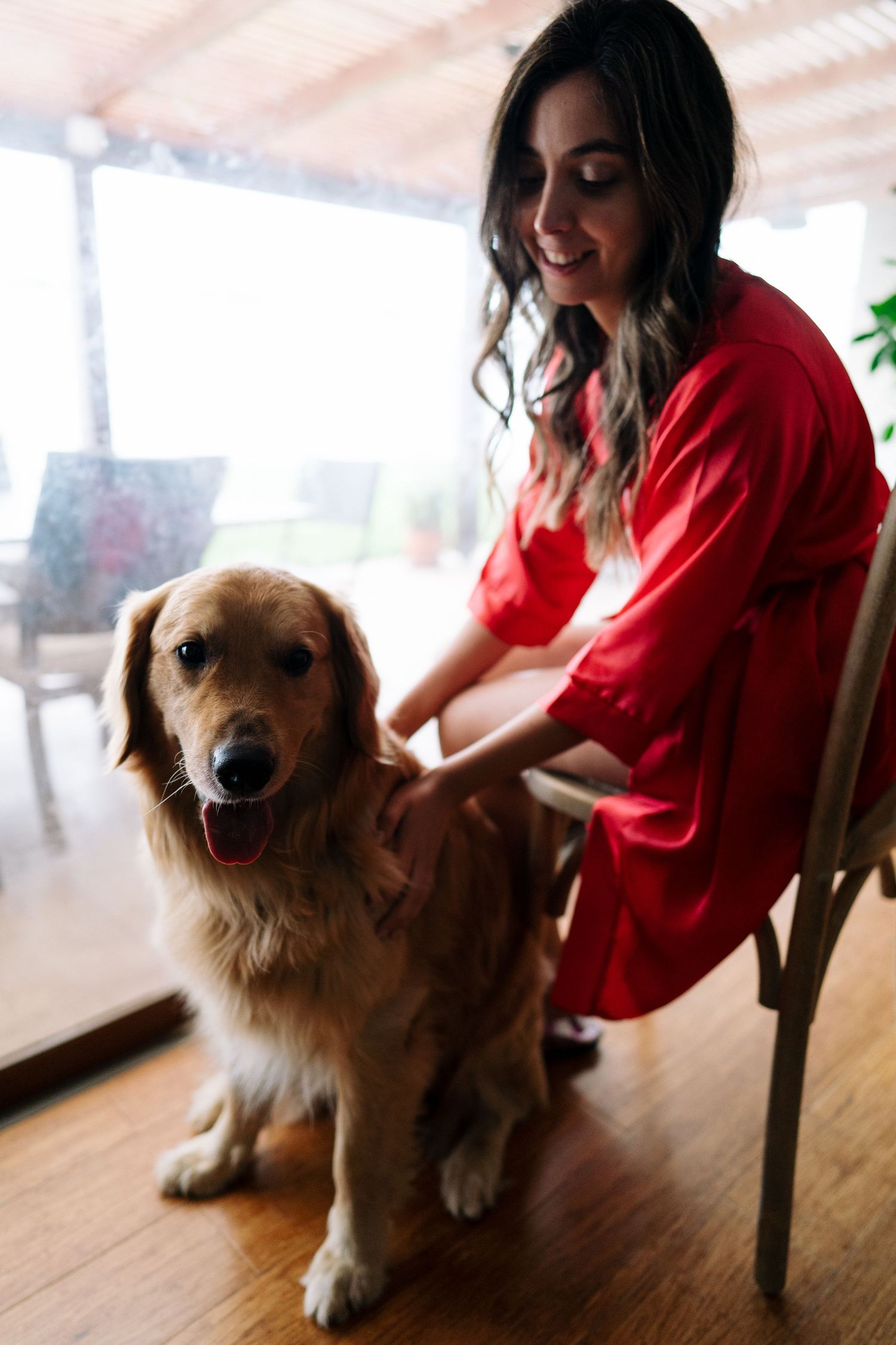 A Golden Retriever poses with someone in a red dress by a covered patio.