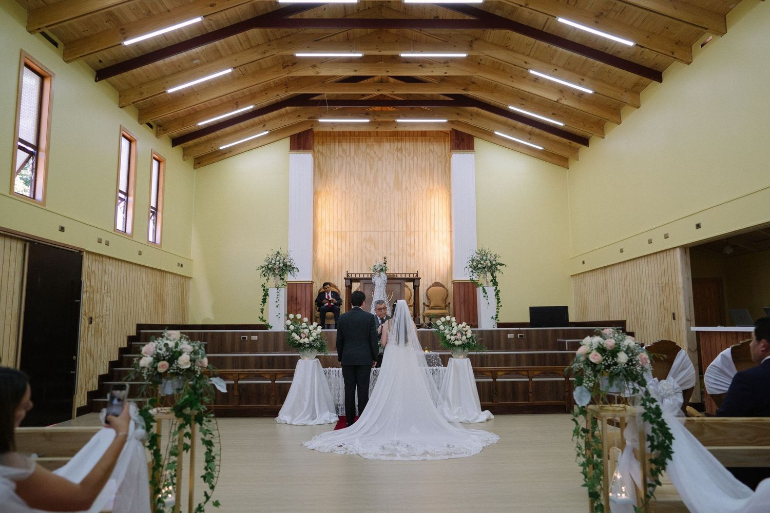 A wedding ceremony in progress inside a church with exposed wooden beams and natural lighting.