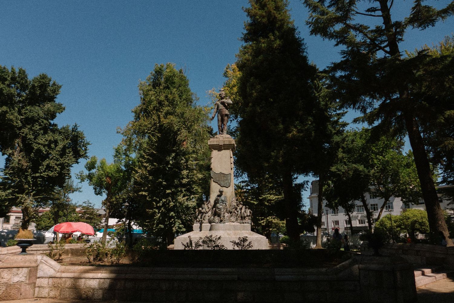 A tall monument stands prominently in a park under bright blue skies.