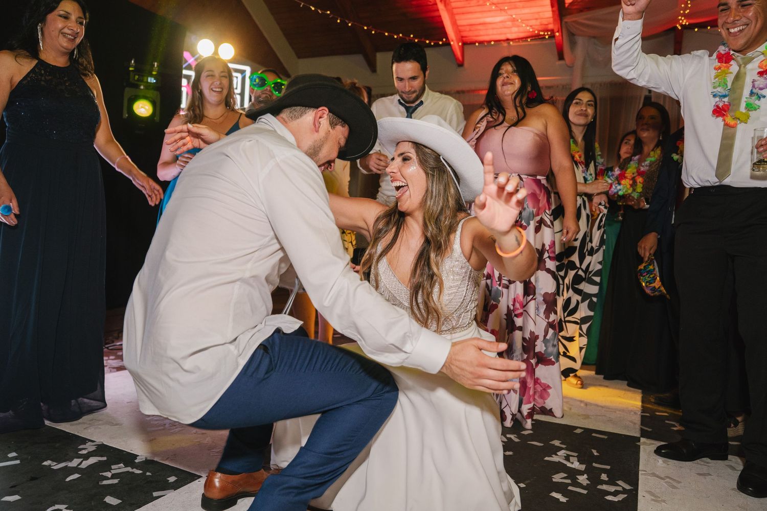 Wedding guests dance and celebrate on a lively dance floor illuminated by string lights during an evening reception.
