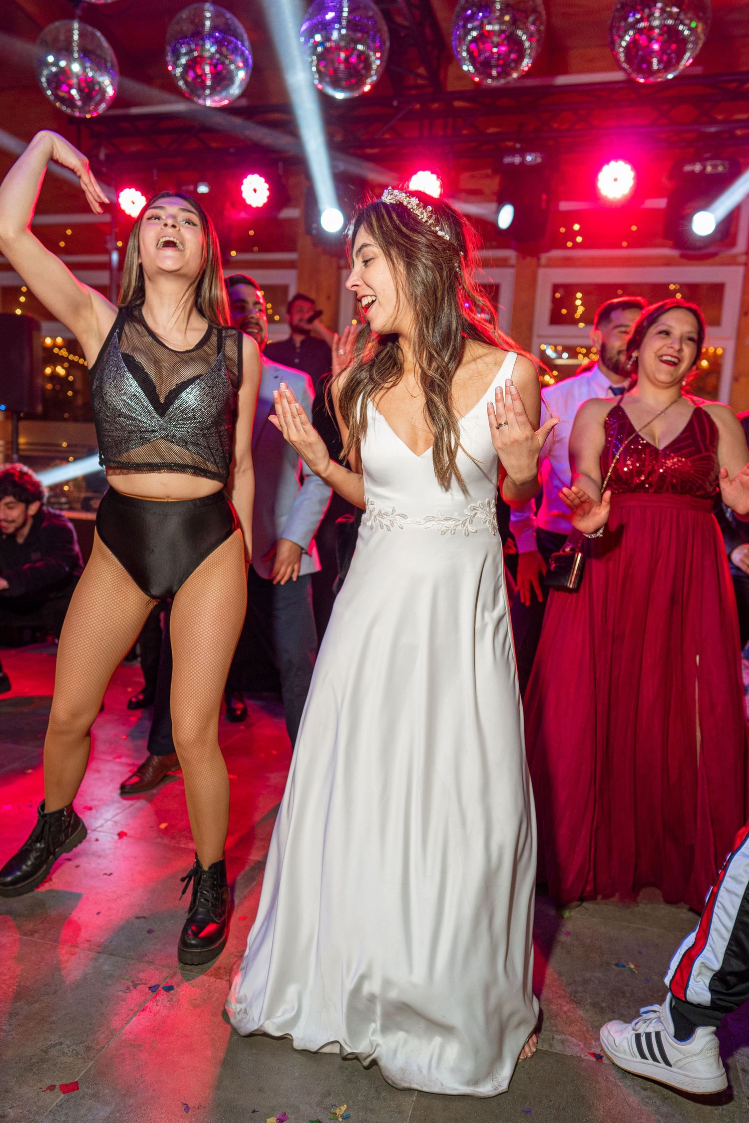 Party guests dancing under red lighting with disco balls overhead during a festive celebration.