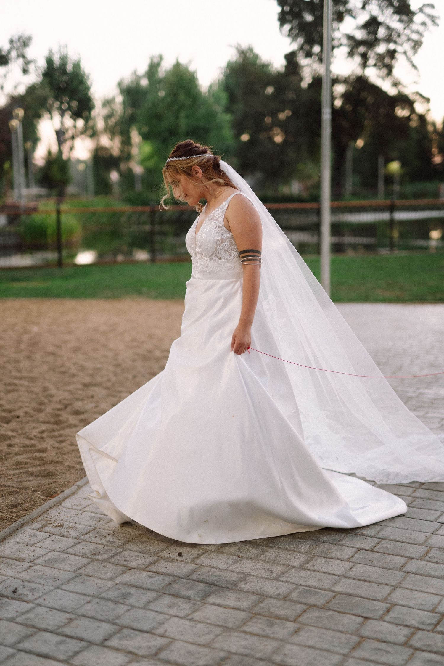 A bride in a lace-detailed dress twirls on a paved pathway, showing off the flowing skirt.