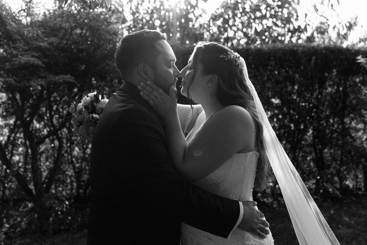 Black and white romantic portrait of newlyweds sharing a tender kiss outdoors.