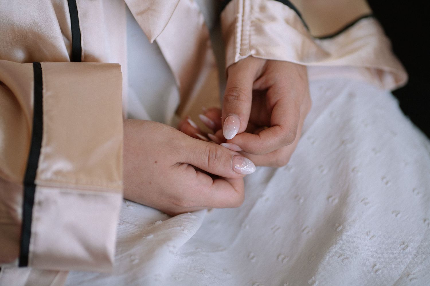 Close-up of hands gently buttoning a white satin garment.