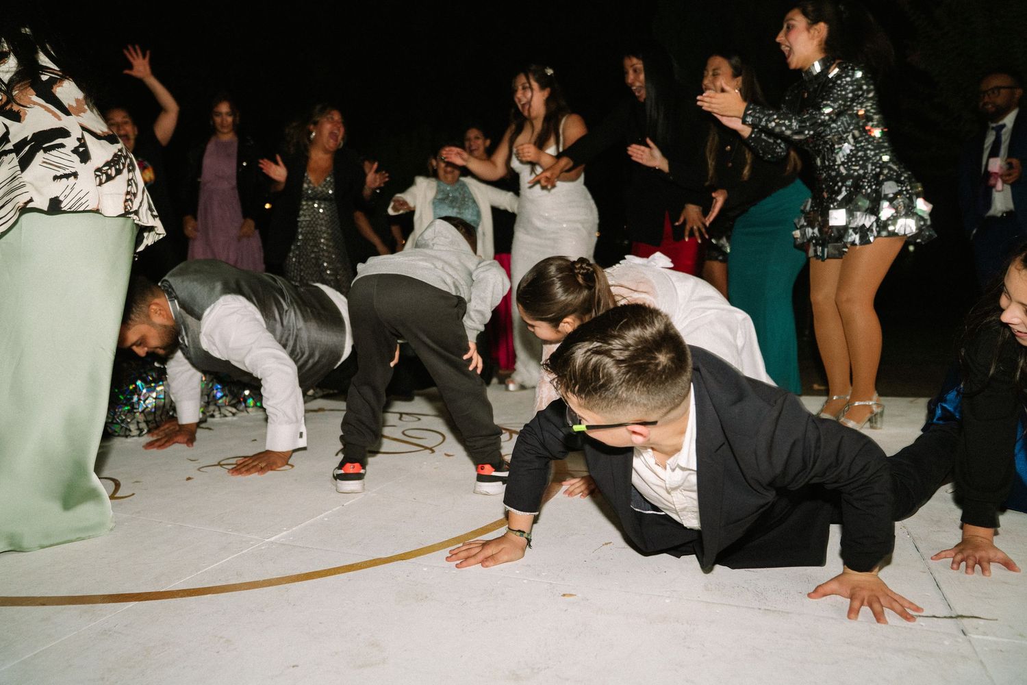 Wedding guests doing push-ups on dance floor during lively and fun outdoor nighttime reception party.