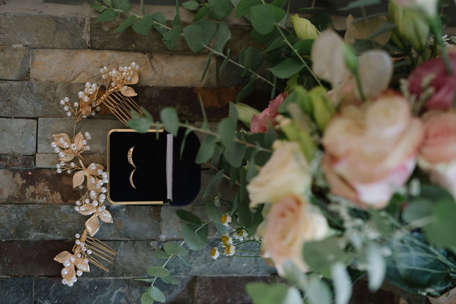 Wedding rings in a black box surrounded by delicate pink flowers and greenery.