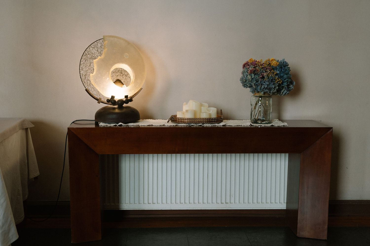 Vintage table lamp and blue hydrangea flowers displayed on wooden console table with radiator.