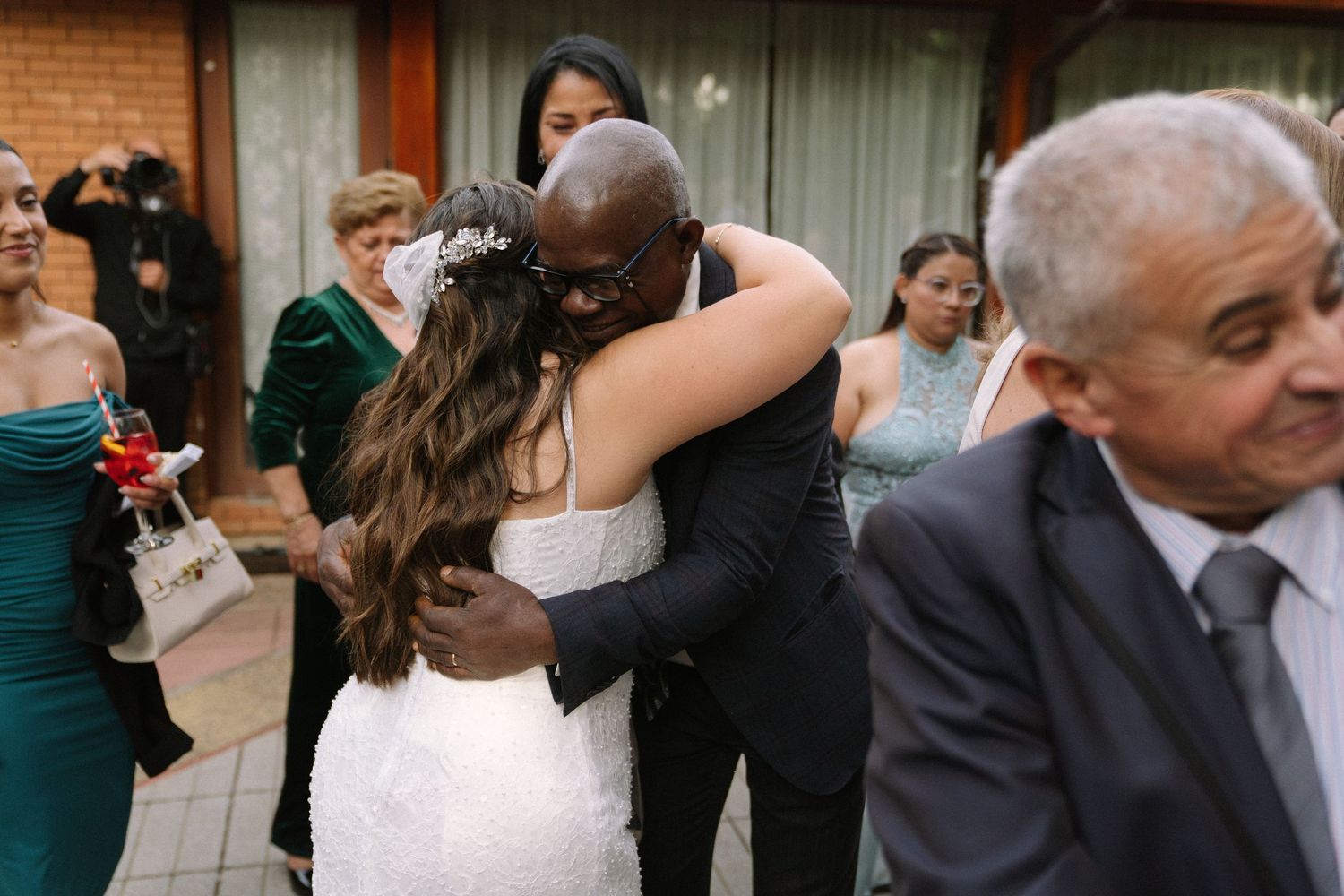 Bride in white wedding dress receives warm hug from guest at outdoor wedding reception.