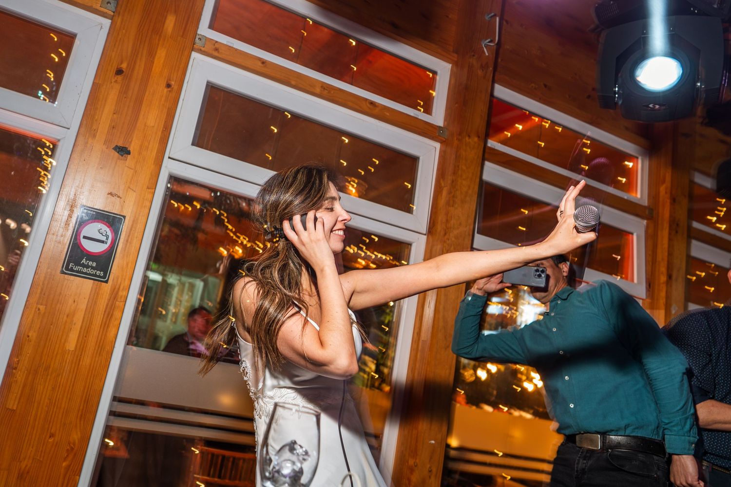 Partygoers dancing enthusiastically beneath wooden beams and string lights.