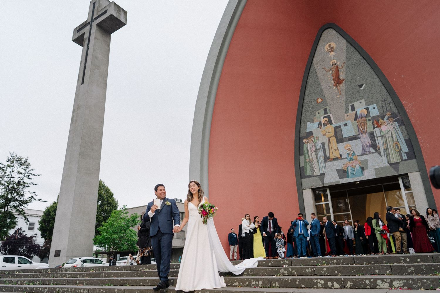 Wedding celebration outside modern church building with dramatic cross tower and architecture.