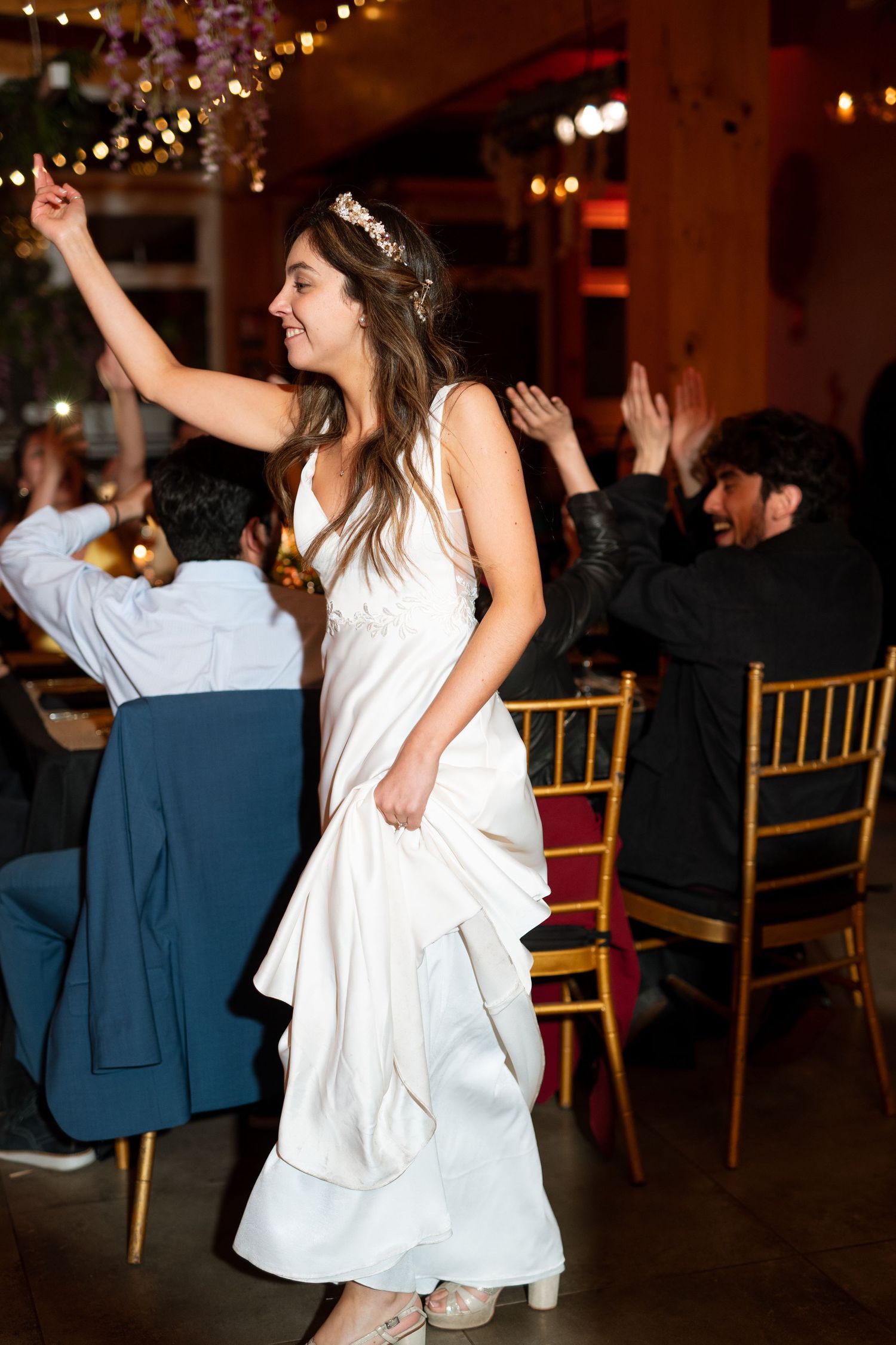 Wedding celebration with person in white dress dancing joyfully among guests at reception.