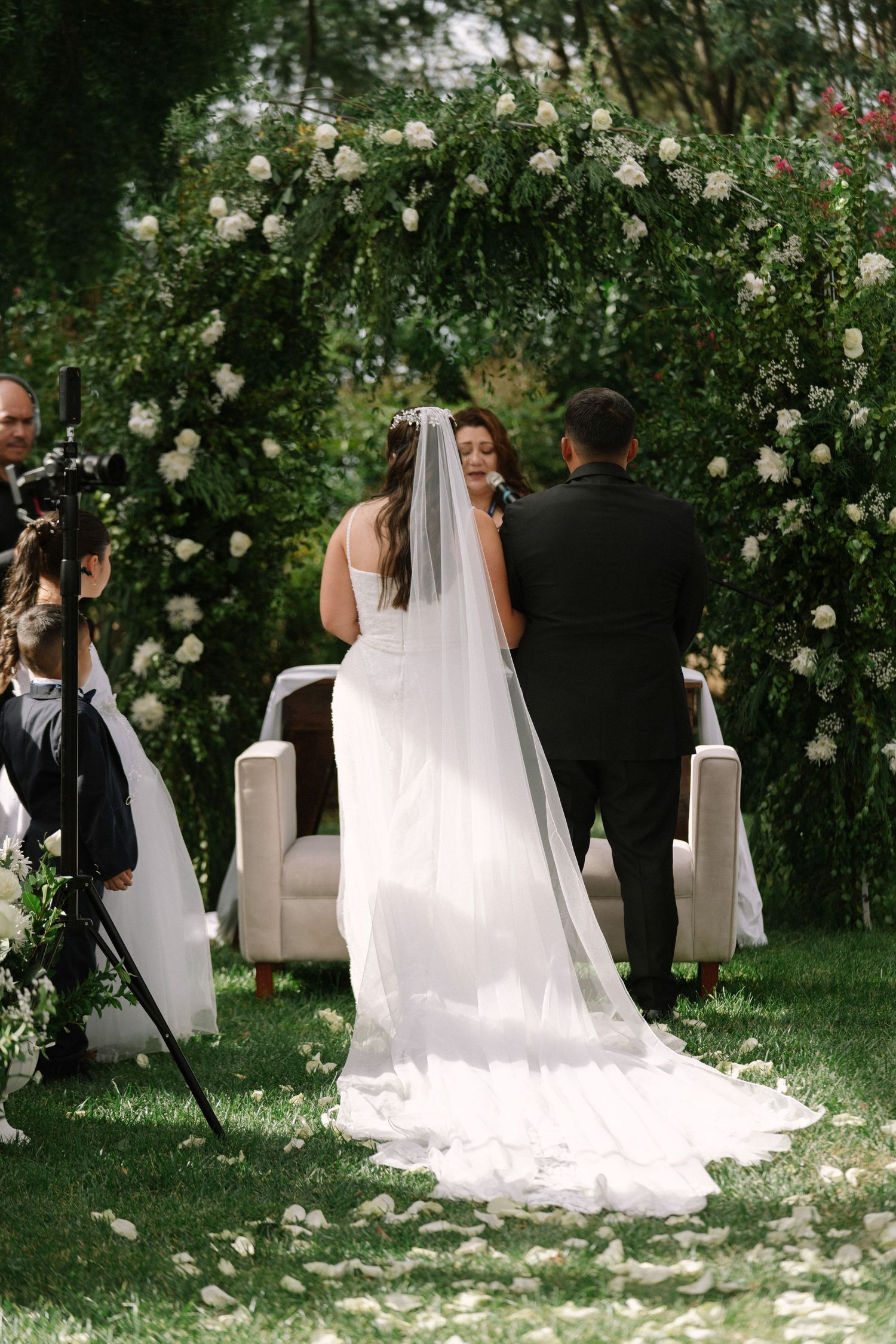 Bride and groom exchanging vows under floral arch at outdoor garden wedding ceremony.