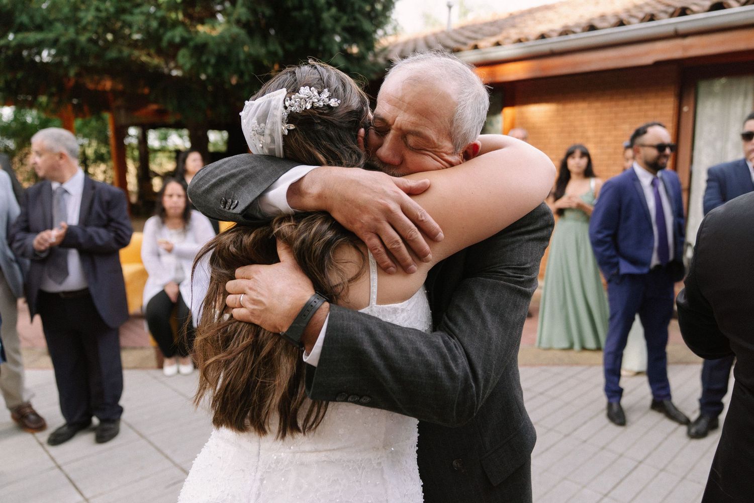 Bride and older man share a warm emotional hug at an outdoor wedding reception venue.