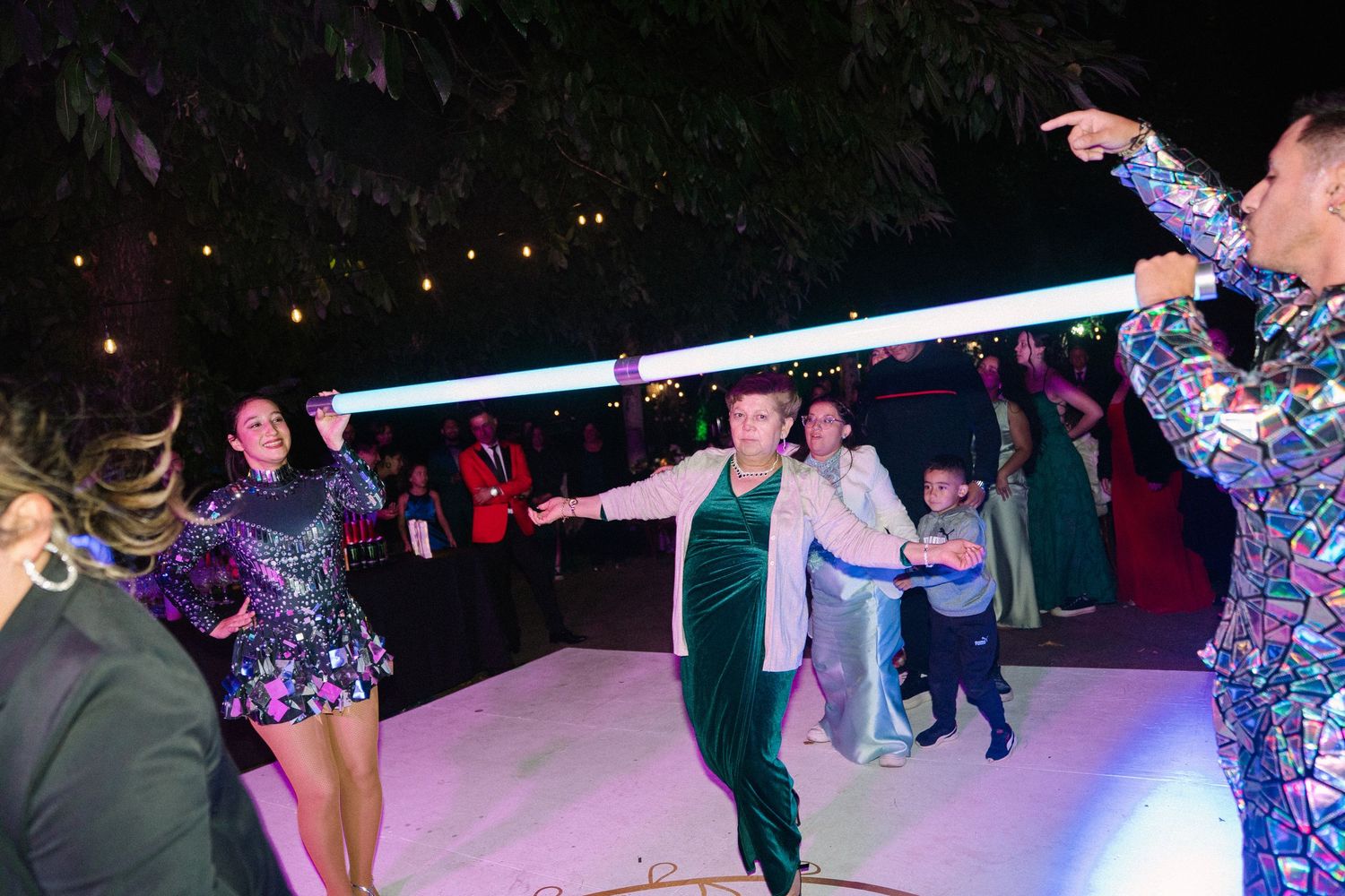Energetic wedding reception dance party with guests in colorful outfits dancing under string lights.