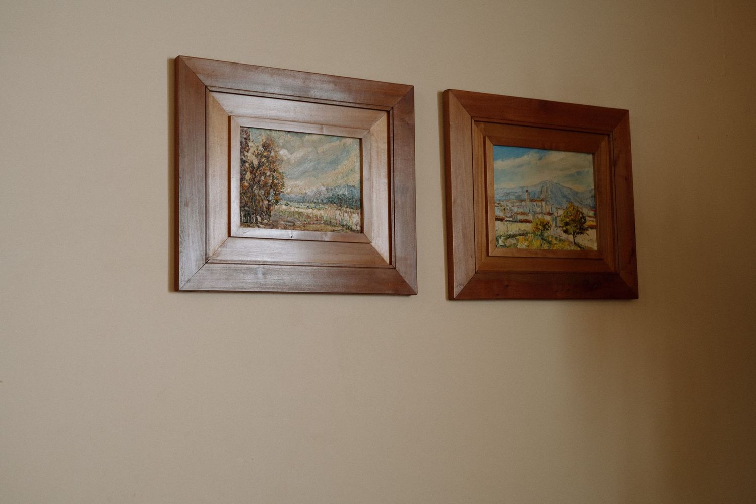 Two vintage landscape paintings in wooden frames hung on beige wall.