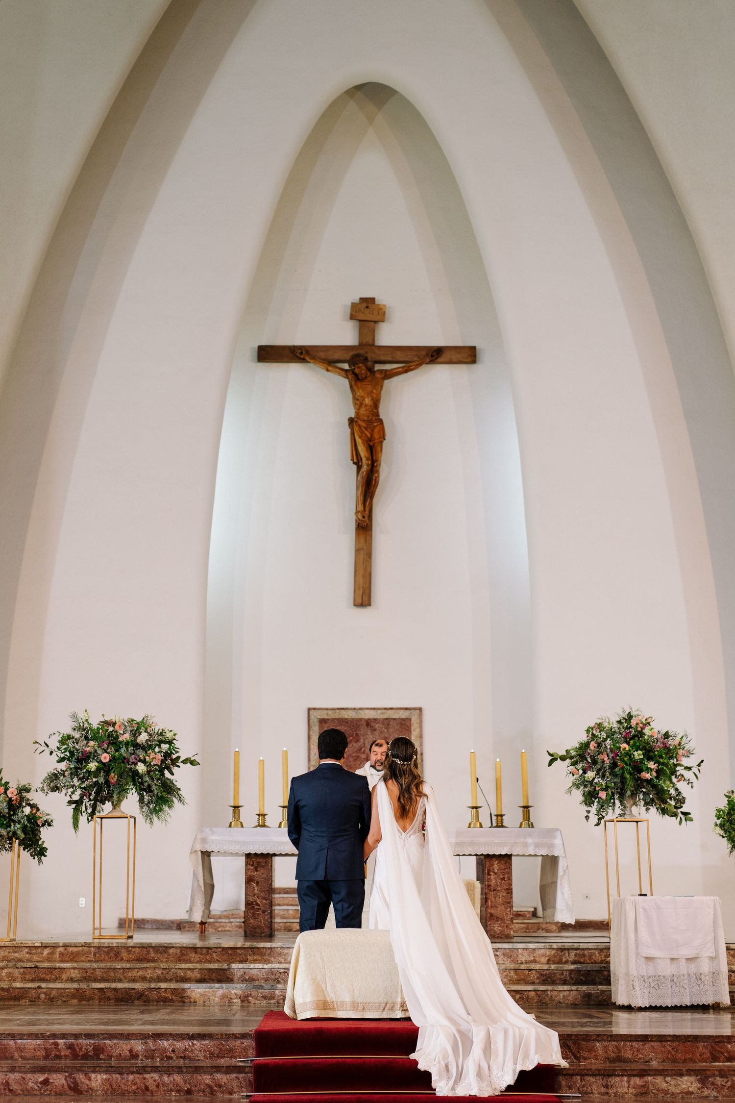 A couple stands at the altar beneath a large crucifix during their church wedding ceremony.