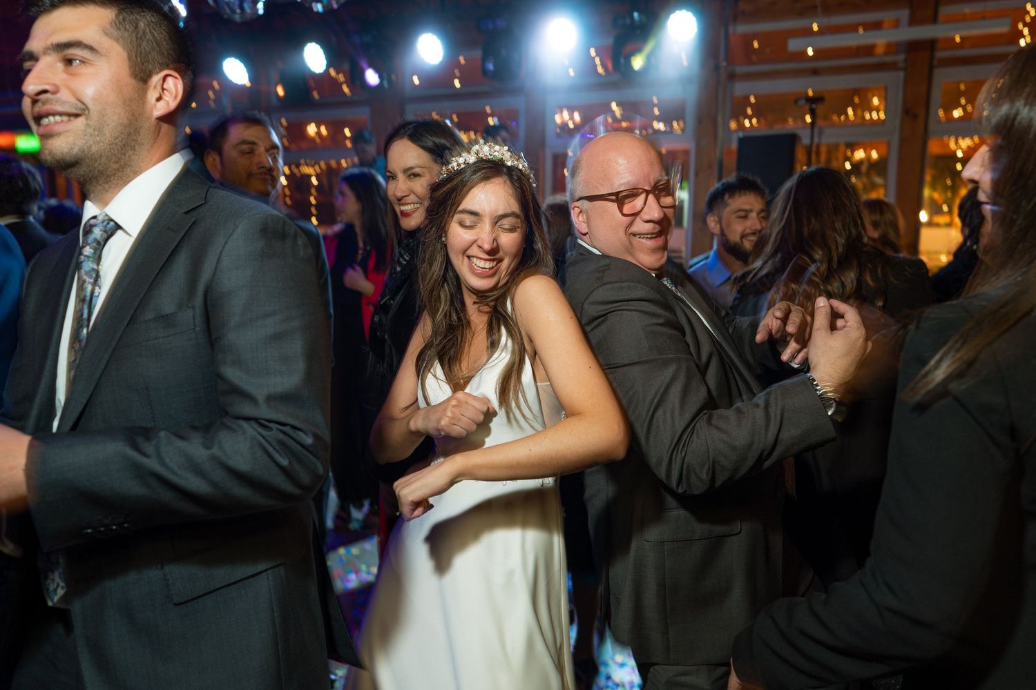 Wedding guests dancing and celebrating at a lively reception with colorful lighting.