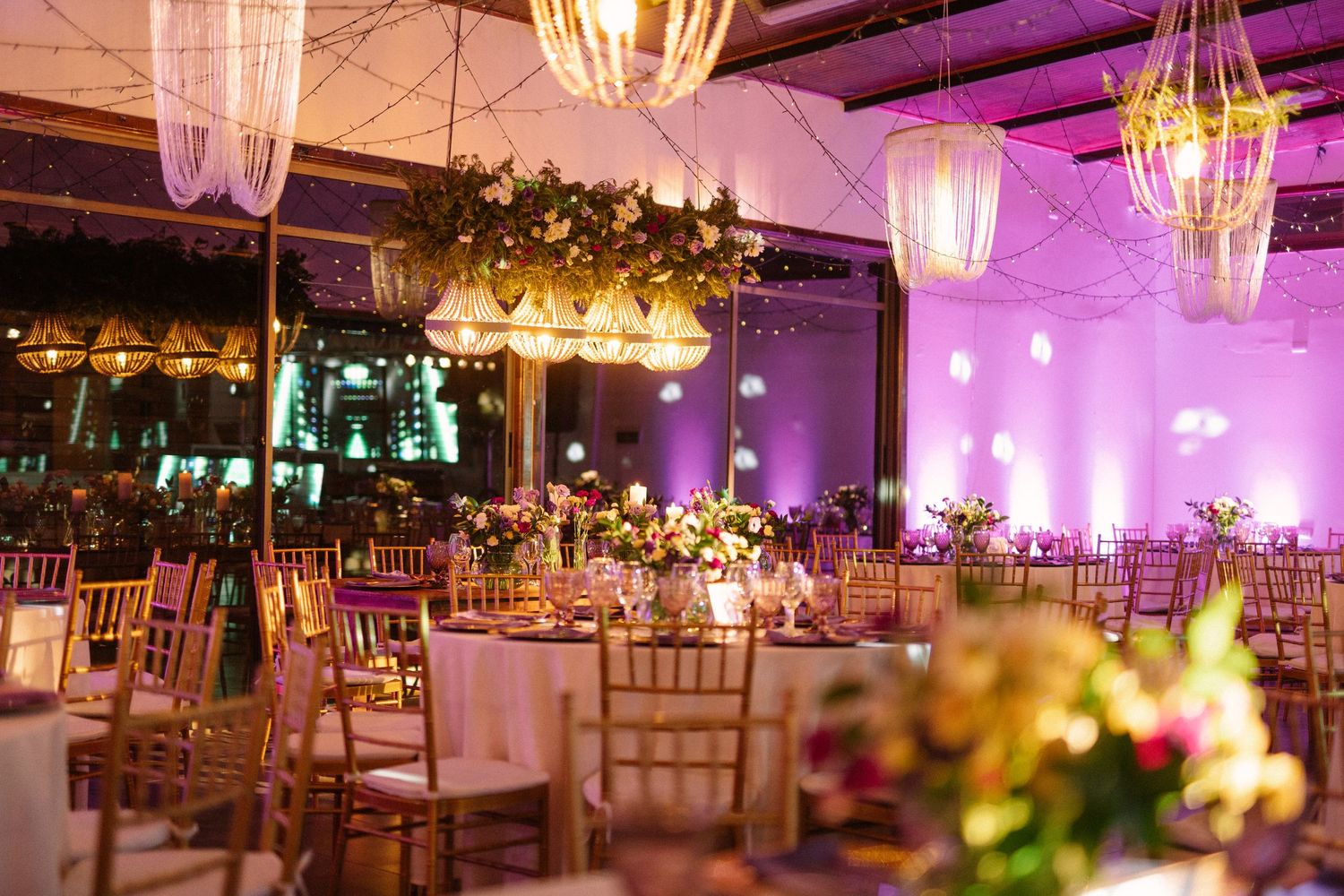 Luxurious wedding reception venue with purple uplighting and crystal chandeliers illuminating elegant table settings.