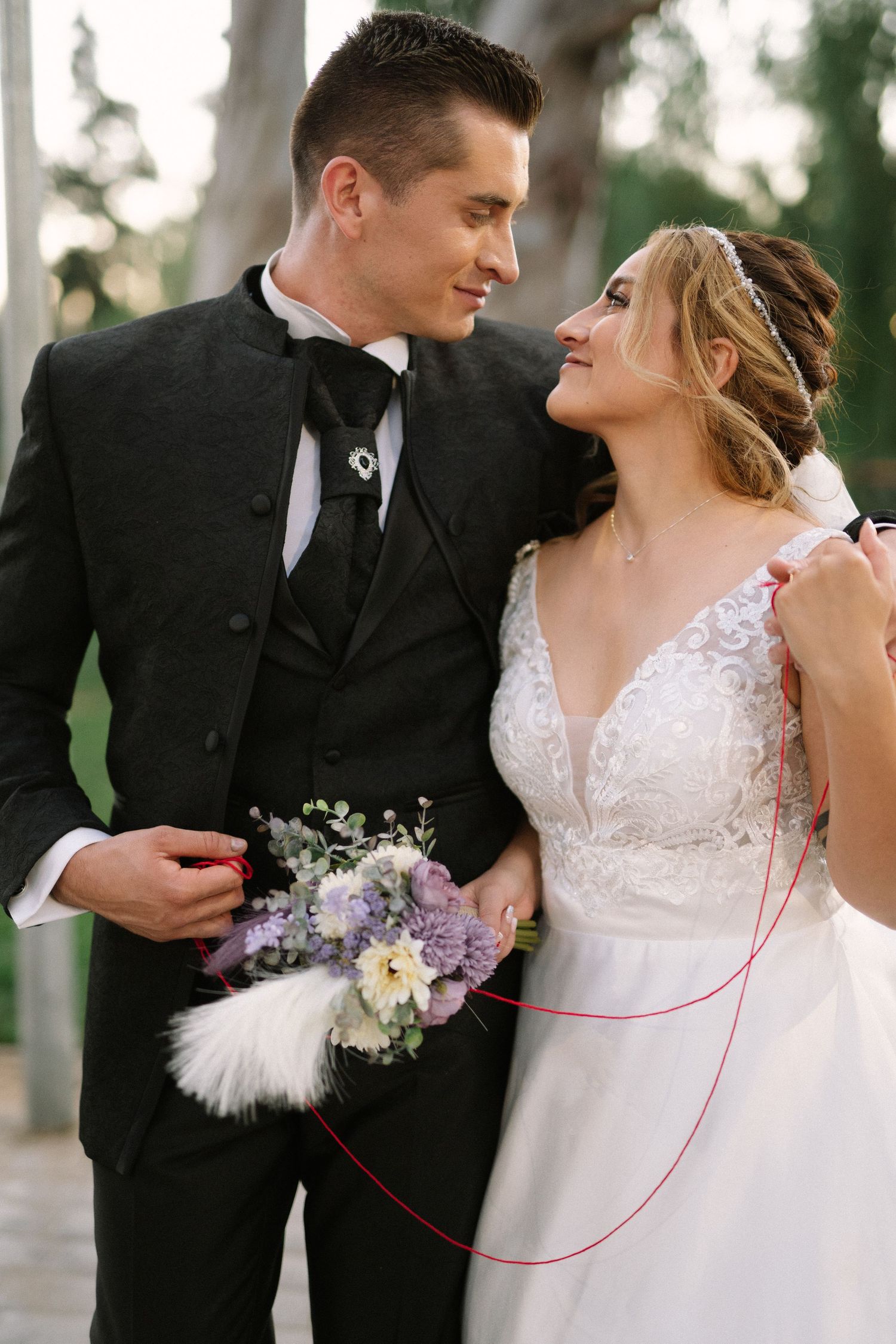 Elegant couple in wedding attire exchange loving glances while holding a delicate bouquet.