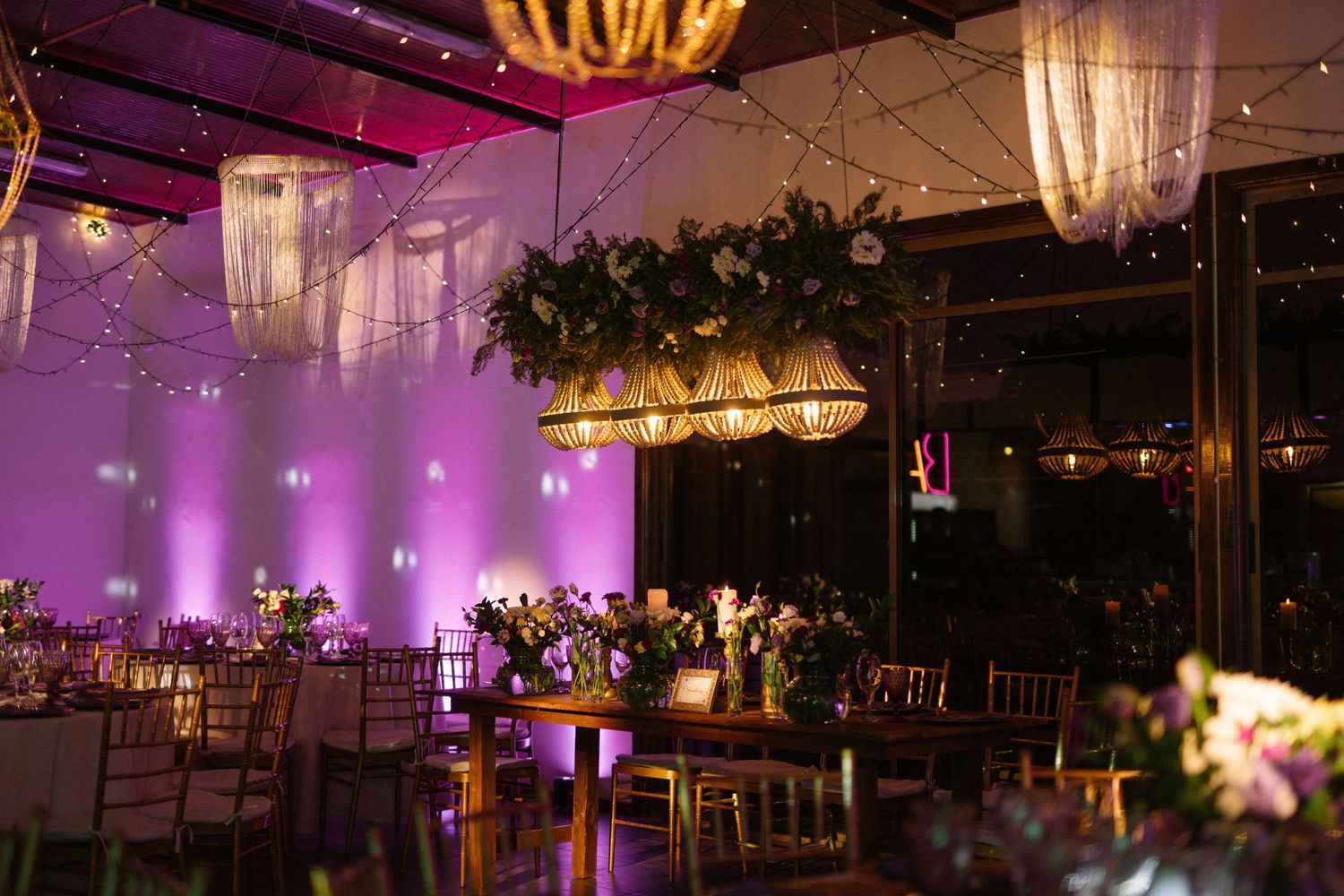 Wedding reception hall with purple ambient lighting, hanging lanterns, and greenery decorations.